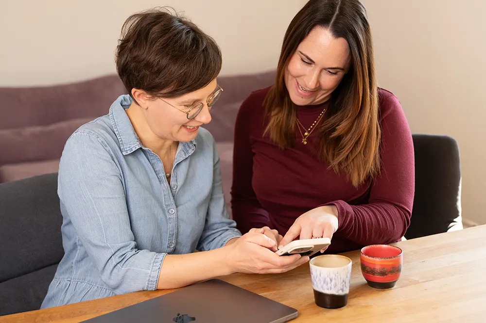 Lena Merz und Annina Schäflein, Mitgründerinnen von Zertovia, schauen gemeinsam auf ein Smartphone